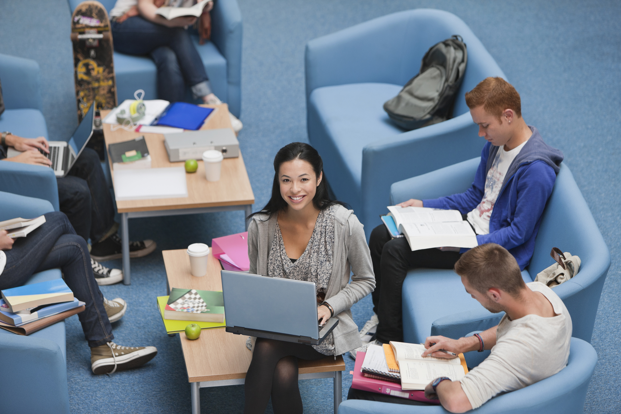 A group of students sit on chairs working on laptops.