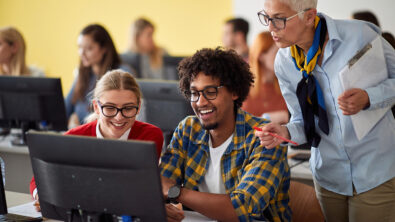 Two students and an instructor look at a computer screen and smile together.