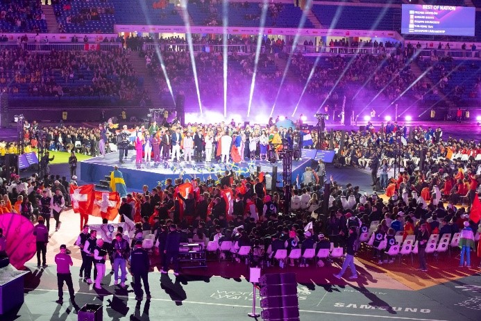 A group of winners stand on a podium in front of a crowd during the closing ceremony at WorldSkills Lyon 2024.