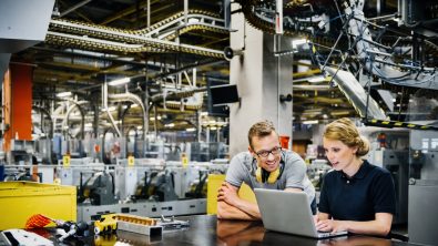 two younger engineers working on laptop in the packing line of a large printery