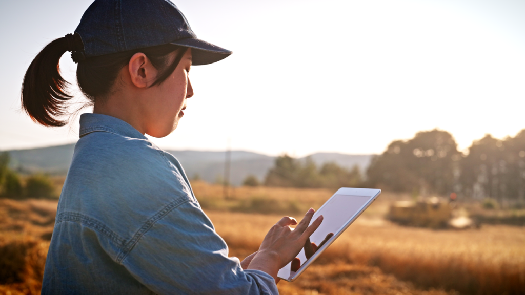 Woman controlling farm equipment from a mobile device. Illustrates software-defined products for heavy equipment.