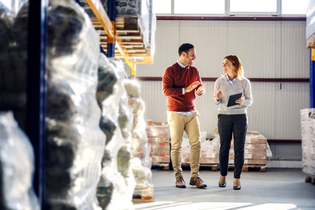 Two business colleagues walking and talking in a busy warehouse during to support supplier collaboration message.