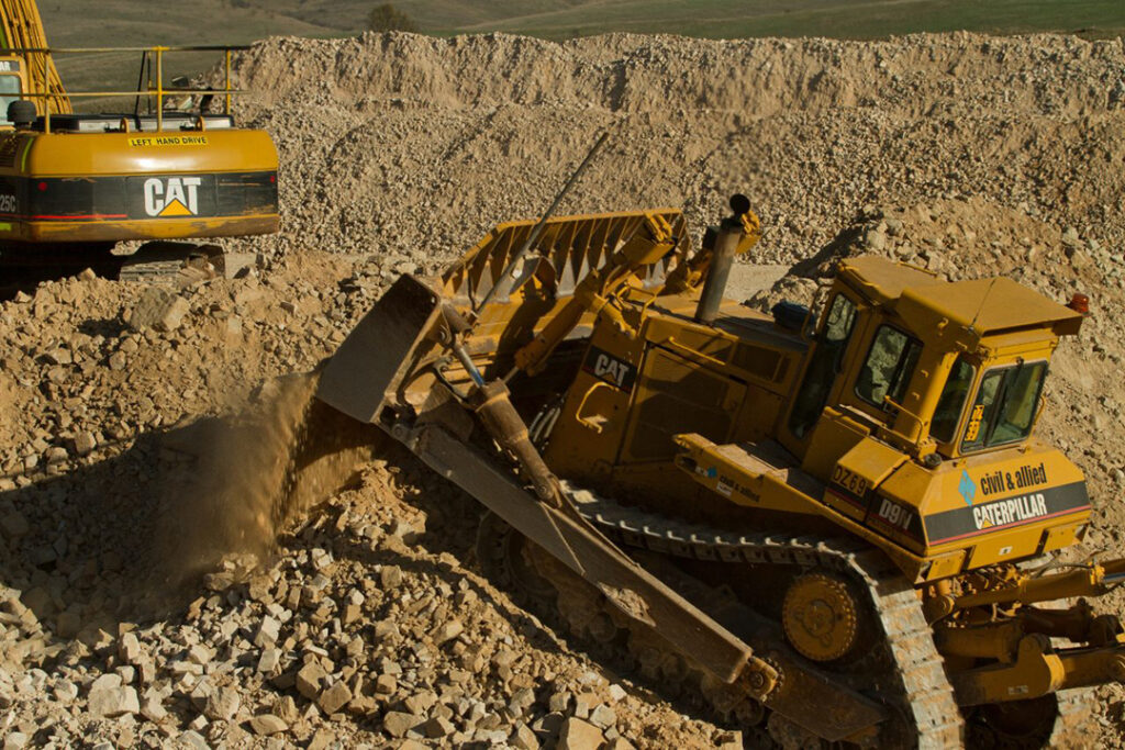 Image of a bulldozer, made up of thousands of heavy equipment parts, moving debris on a construction site. 