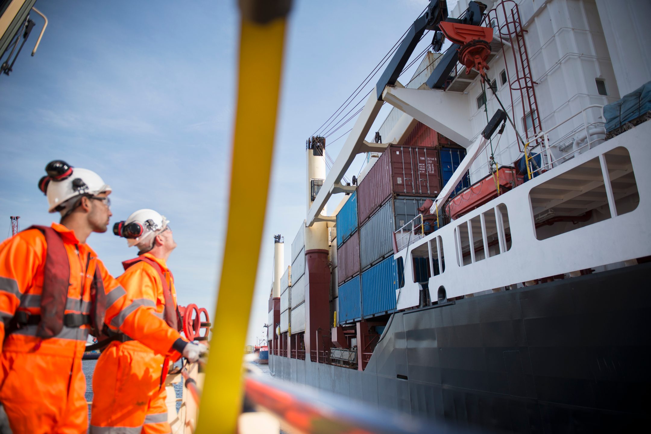 A pair of tug workers stare up at a docked container ship.