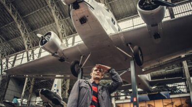 A man standing beneath an old plane suspended in a museum.