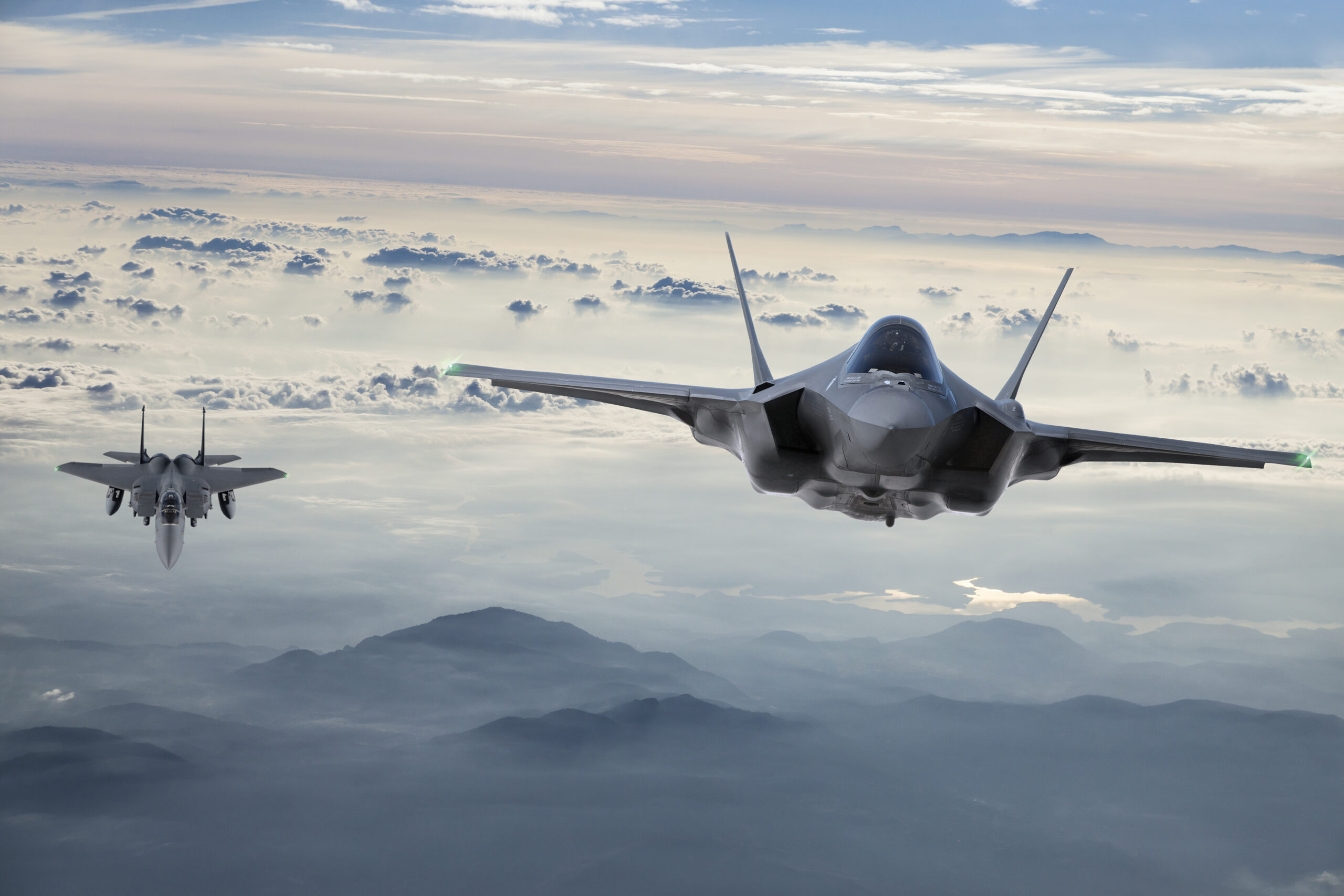Two fighter jets flying above a mountainous landscape.