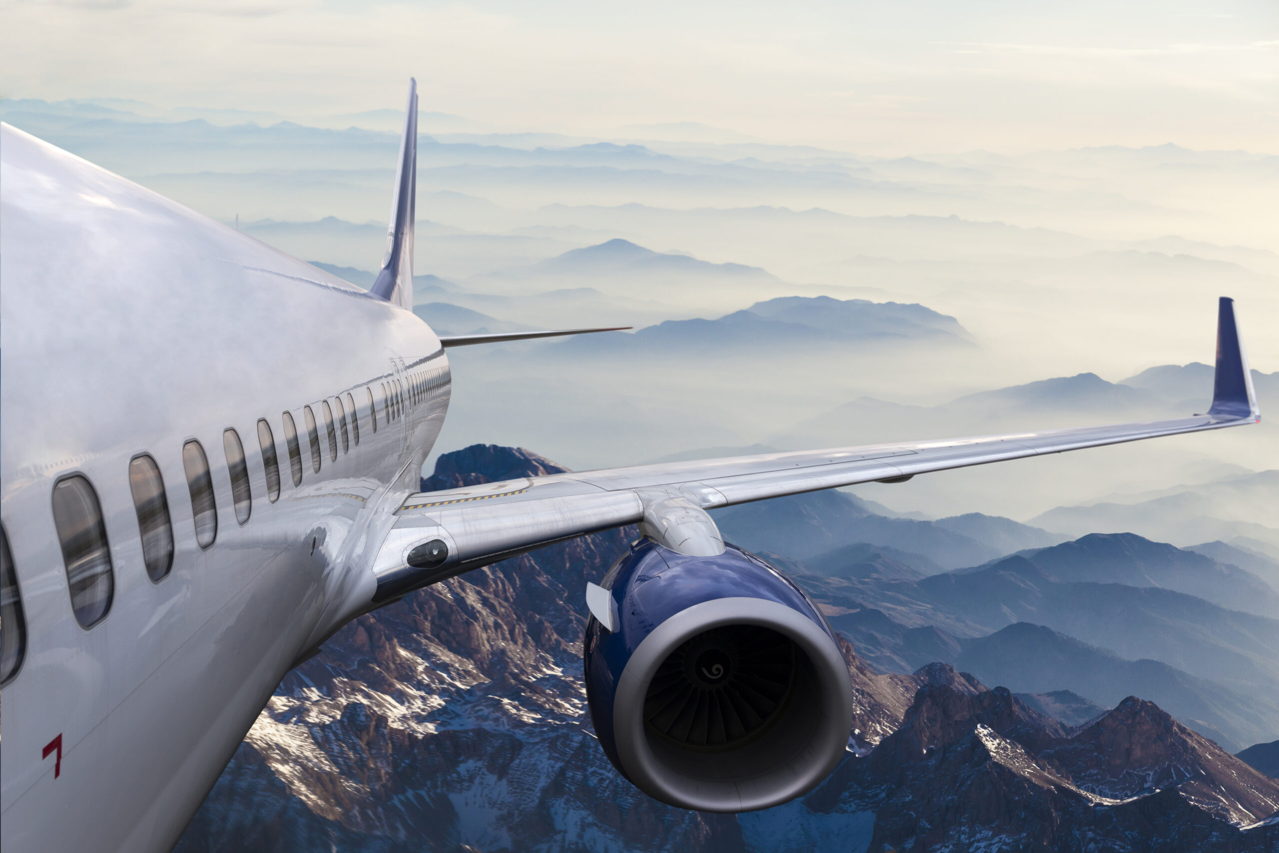 The body and wing of an airplane flying above a mountainous landscape.