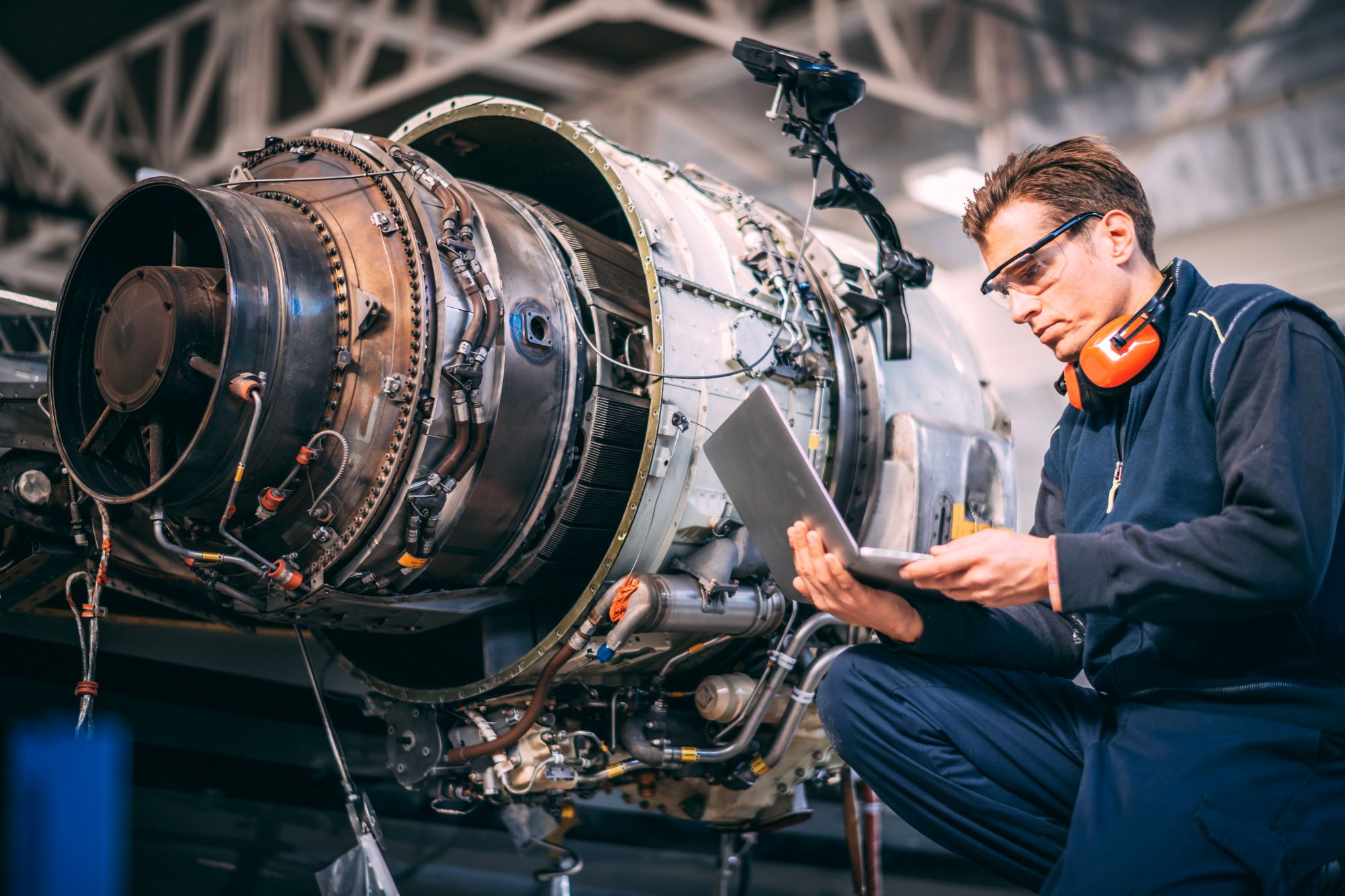 An aerospace engineering working on a laptop next to an aircraft engine.