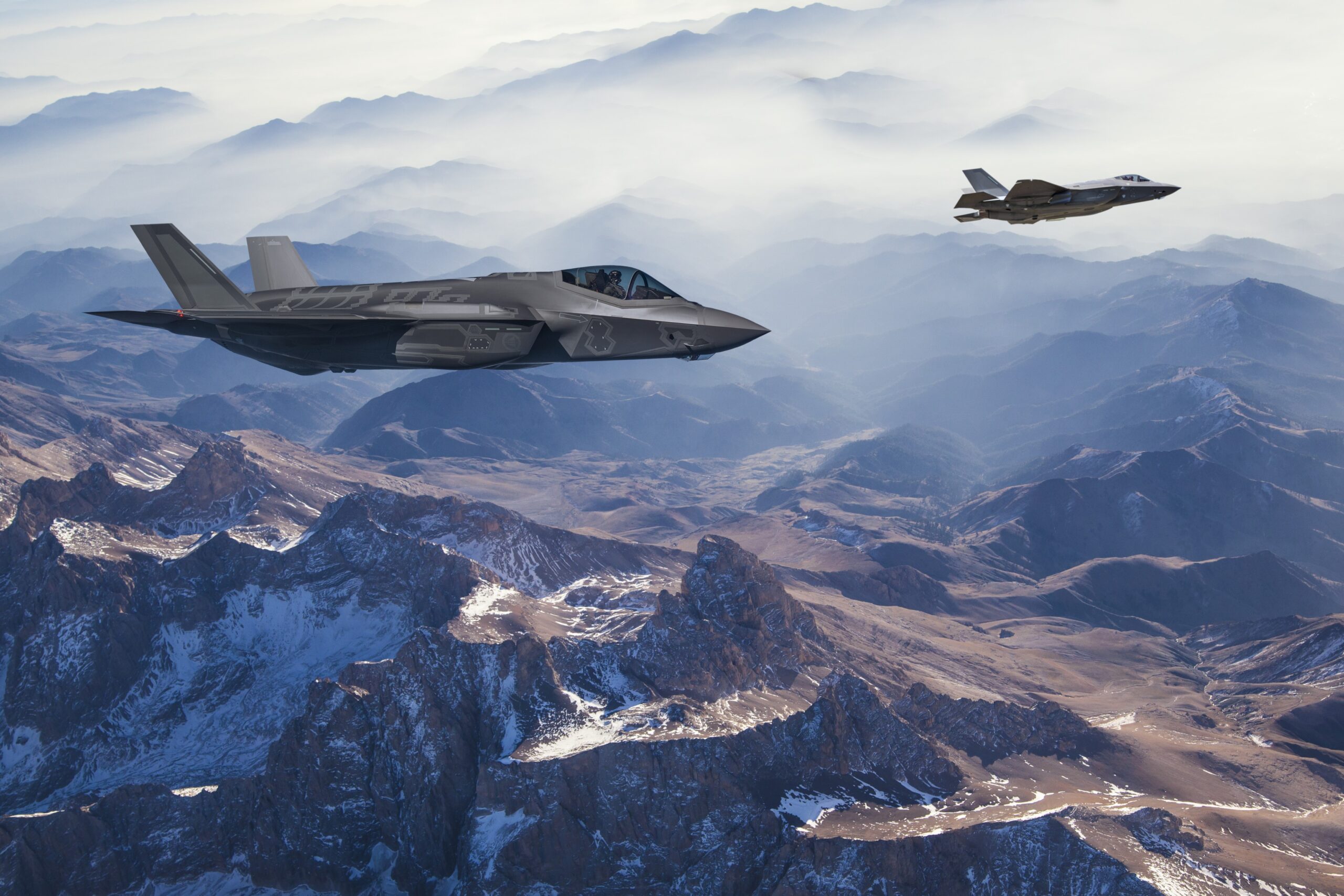 Two fighter jets flying high above a mountainous landscape.
