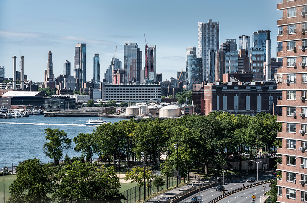 The skyline of New York City behind a riverside park, in the bright daylight.