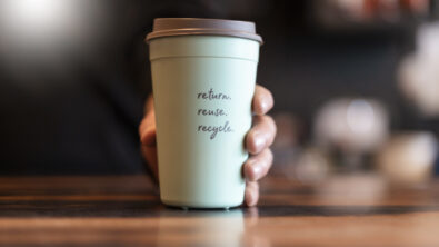 Close-up of a hand holding a cup that says "Return, reuse, recycle."