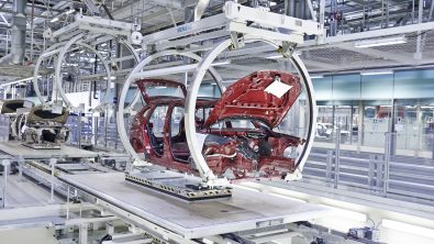 A red car chassis being assembled in a robotic assembly line inside a white factory.