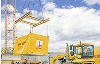 A yellow shipping container with a module for modular construction being placed onto a truck by a crane.