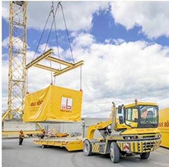 A yellow shipping container with a module for modular construction being placed onto a truck by a crane.