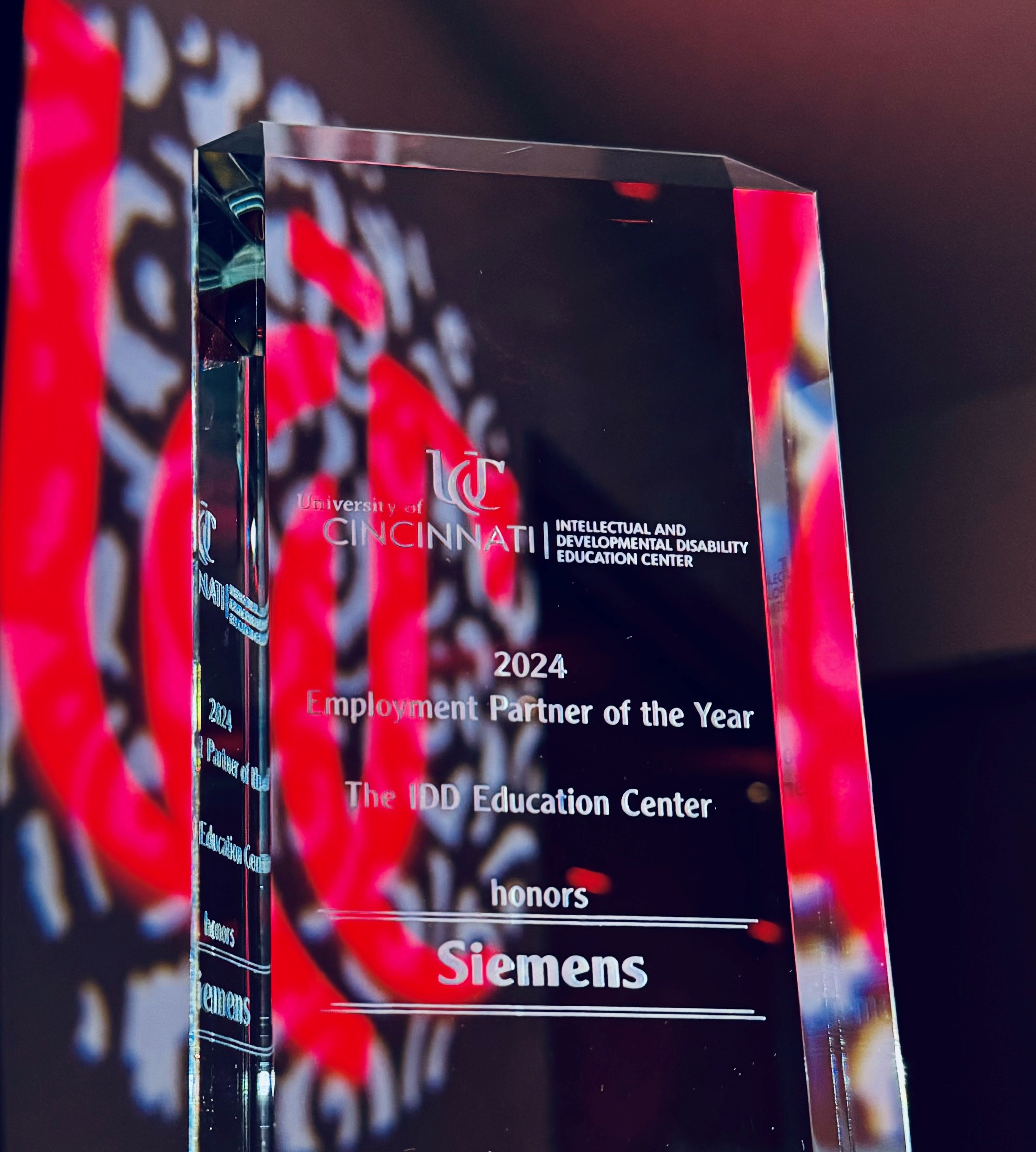 A glass "Employment Partner of the Year" award addressed to Siemens in front of a University of Cincinnati "UC" logo.