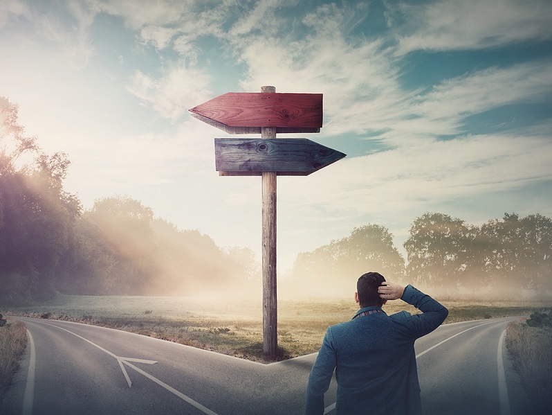 Businessman in front of crossroad and signpost arrows shows two different courses, left and right direction to choose. Road splits in distinct direction ways.