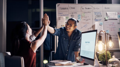A man and woman in a modern office setting high five in celebration of an achievement. S&T partners can work with traditional channel partners to win more deals.