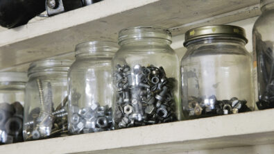 A shelf holding several jars of nuts, bolts and screws. Searching for parts can be a cumbersome and time-consuming, like sifting through jars of old bolts looking for the right one.