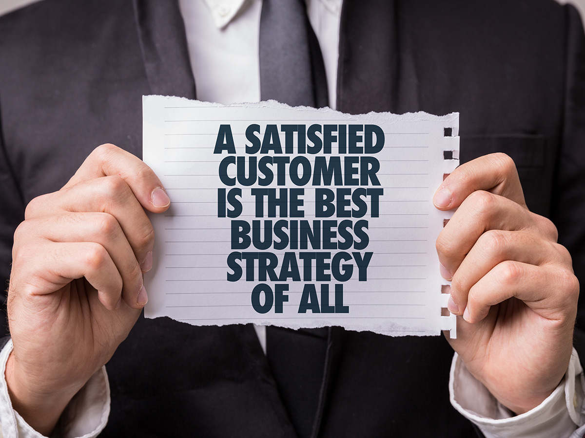 A man holds a small piece of paper that has the words "A satisfied customer is the best business strategy of all" printed on it.