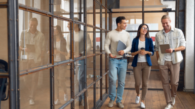 three people walk down a hallway. they are flanked by a glass wall