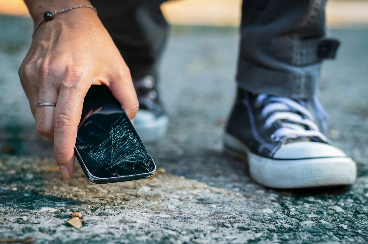 person picking up cell phone with cracked screen from the sidewalk after dropping it