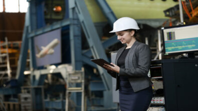 A woman in a hard hat in an airplane manufacturing shop examines a tablet