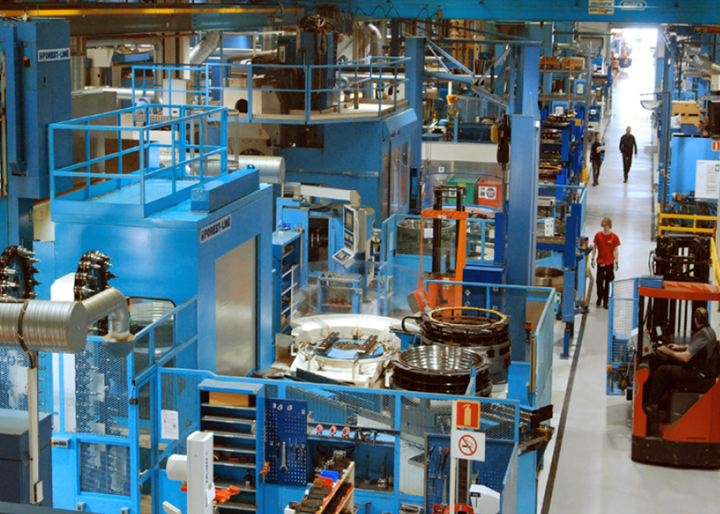 large factory with people walking through and blue and orange metal machines