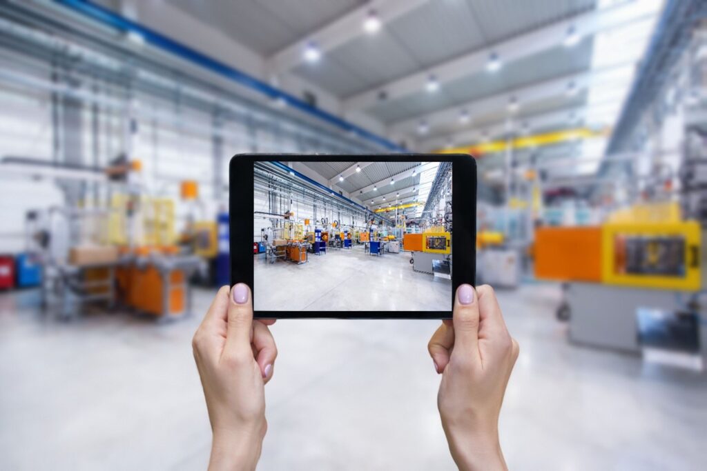 A pair of hands holding a tablet and looking at a manufacturing floor.