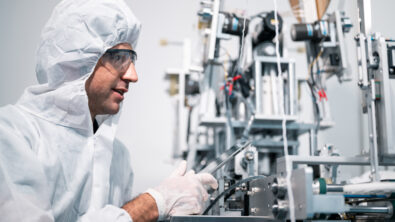 Scientist wearing protective clothing working on a machine in a medical device manufacturing facility.
