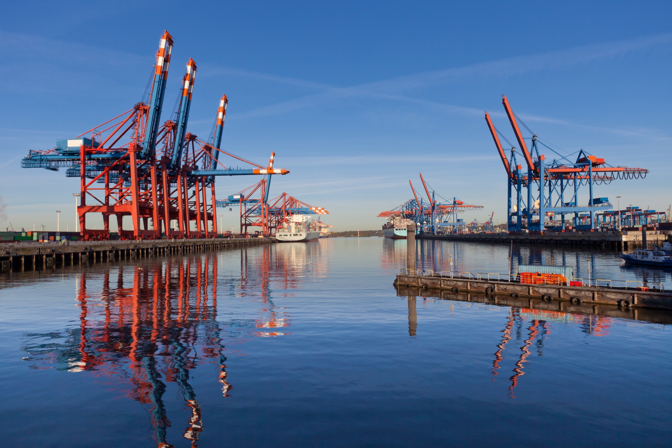 Two lines of cranes separated by a body of water in a harbor.
