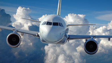 Front view of a commercial airplane flying in front of a cloud-filled background.