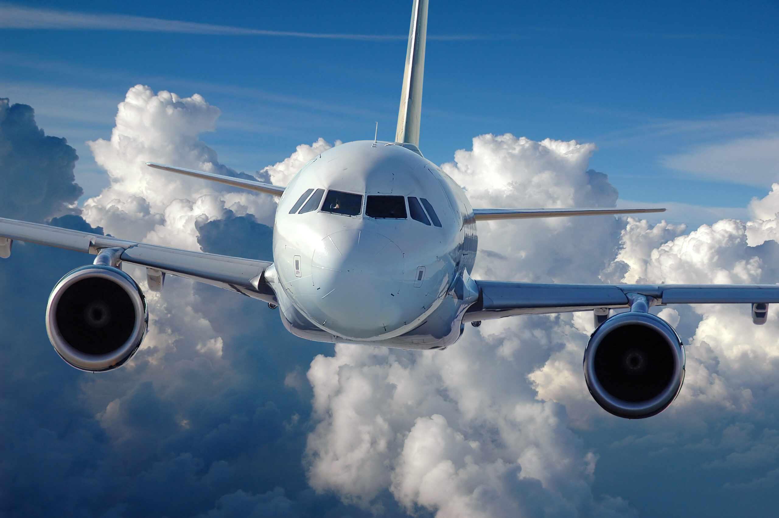 Front view of a commercial airplane flying in front of a cloud-filled background.