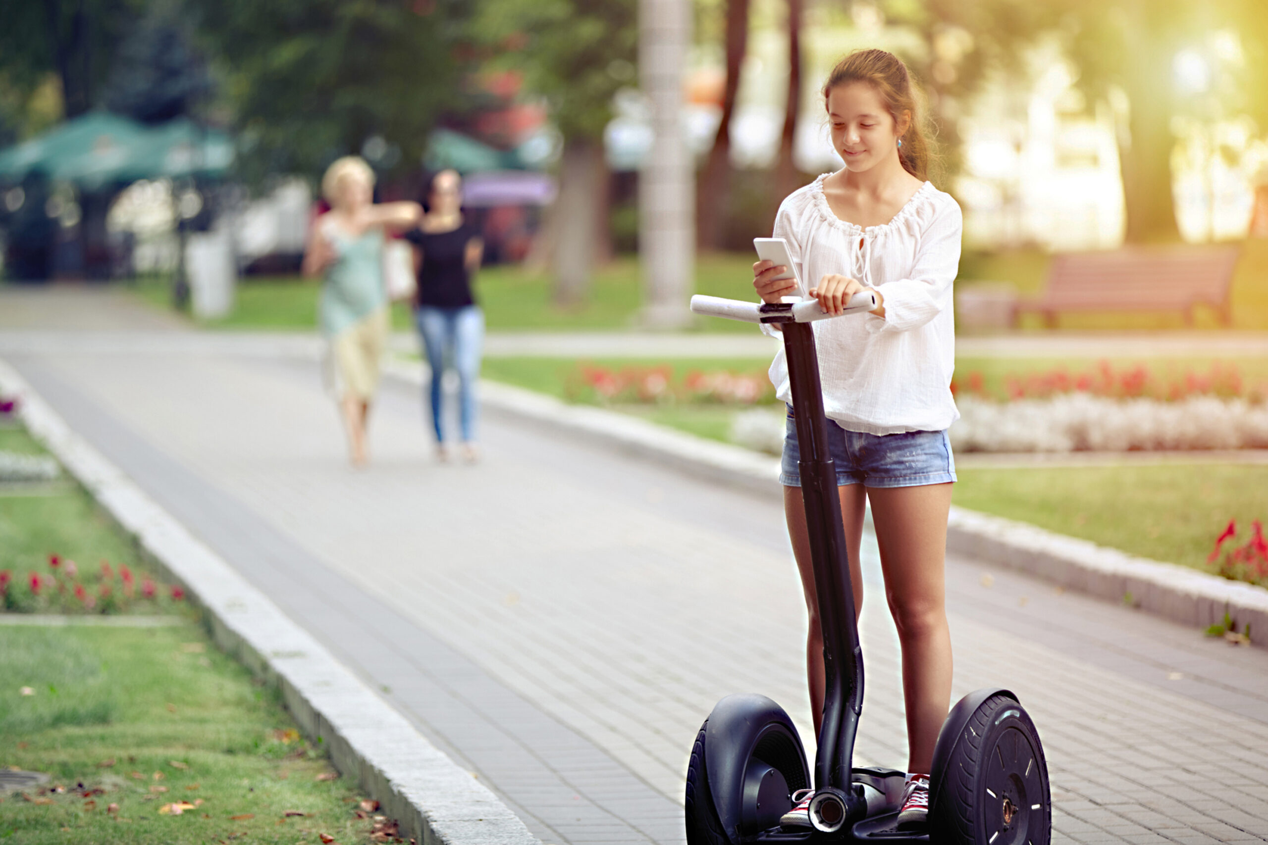 A young girl with a smartphone is riding a segway that was made with smart manufacturing.