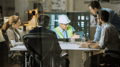 Four engineers sitting at a desk watching an engineer with holding tablet on a large computer screen
