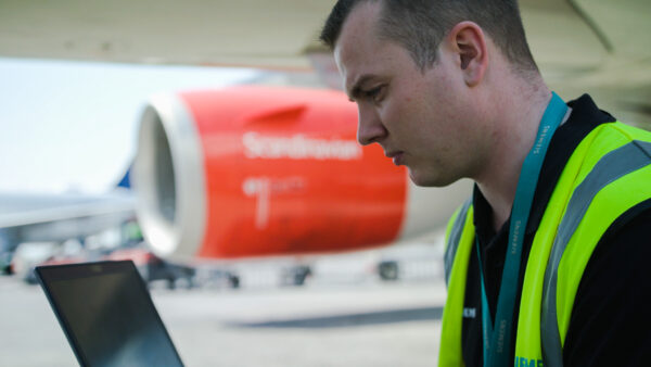 Technician on airplane runway checking service software to show maintenance forecasting.