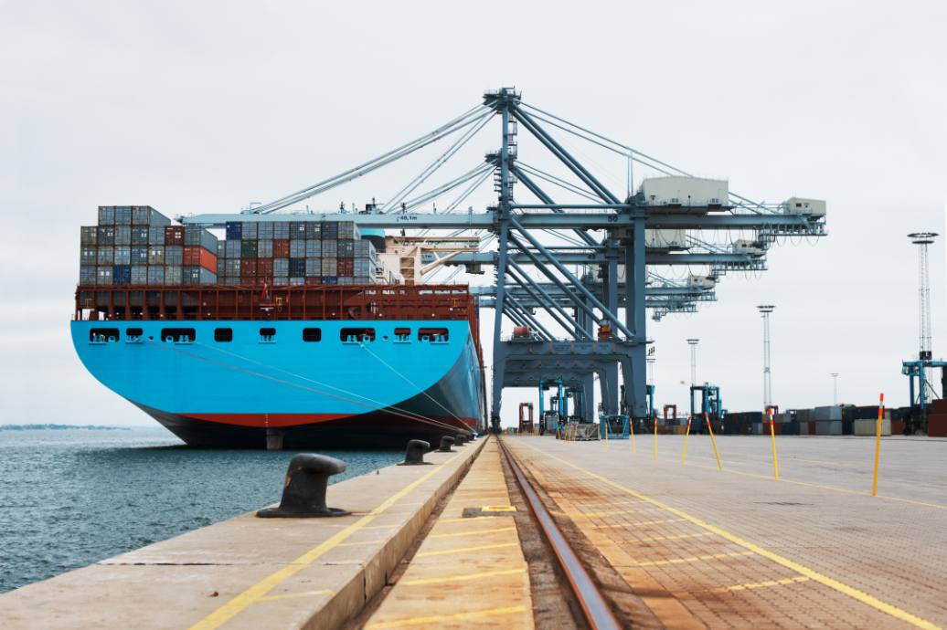 A massive blue ship with cargo being loaded on to it with cranes