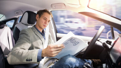Caucasian driver reading magazine in autonomous car. Self driving vehicle. Driverless car.