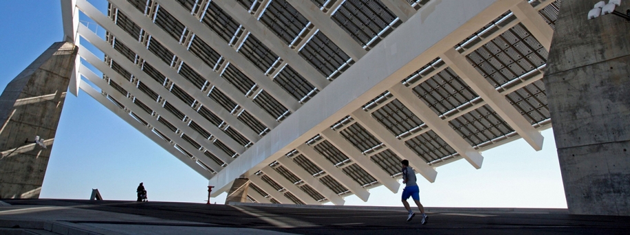 Runner running under a large, urban solar power panel