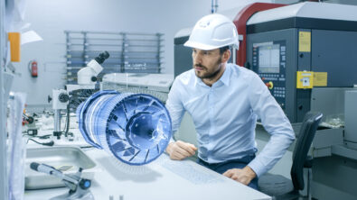 Bussiness man wearing a hardhat works with holographic projection 3D model of a engine turbine prototype.