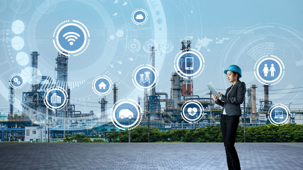 Woman outside of a factory holding a tablet. She is surround by graphical icons representing different technologies and industries.
