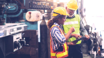 Man and woman in hard hats at a factory looking at a tablet
