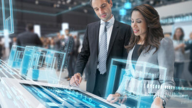 Business woman and man standing at a table-height touch screen. There is a digital overlay of lines and shapes representing a technological network