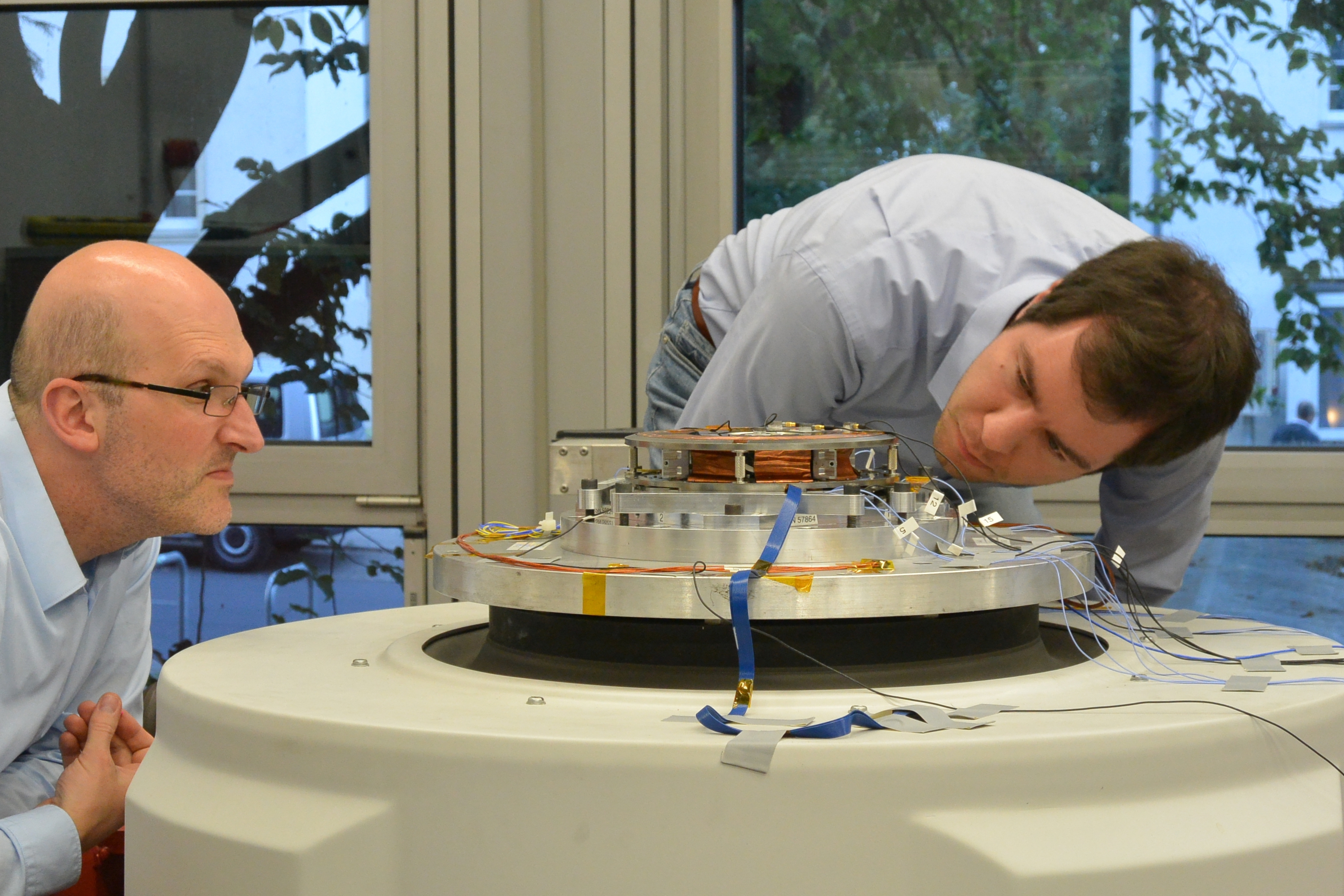RWTH professors and future engineers examine a satellite piece fitted on a shaker table