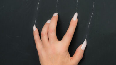 Mature woman scratches the blackboard with her long nails leaving scratch marks on the blackboard