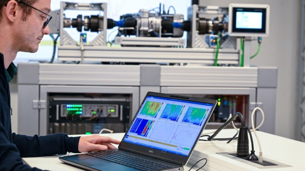 Trained HV safety engineer analyzing time-aligned multi-physics measurements from electric drivetrain setup using Simcenter Testlab software, with Simcenter SCADAS hardware visible in the background
