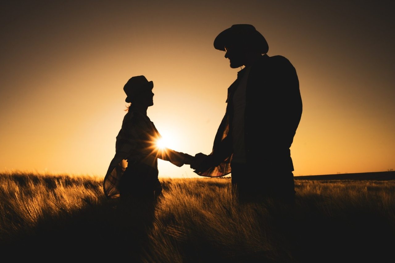 Two people standing in a harvested field at sunset discussing agricultural equipment performance.