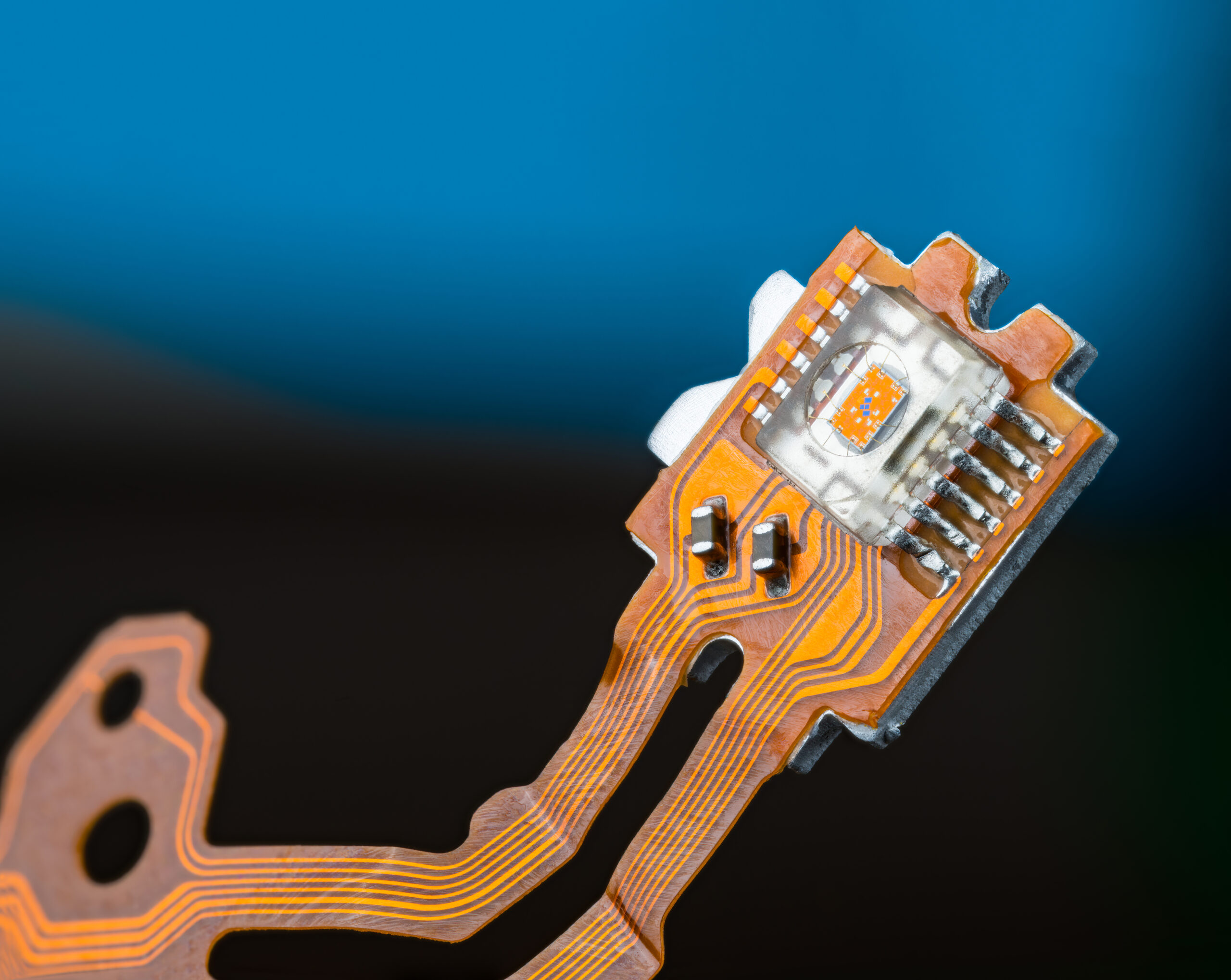 Closeup of optical sensor on electronic printed circuit board and flex ribbon cables on dark blue background