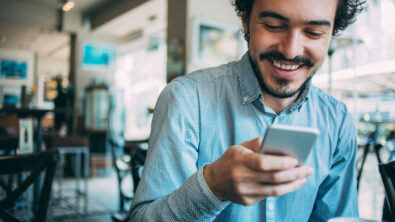 Young man sitting in cafe looking at his smart phone, with copy space.