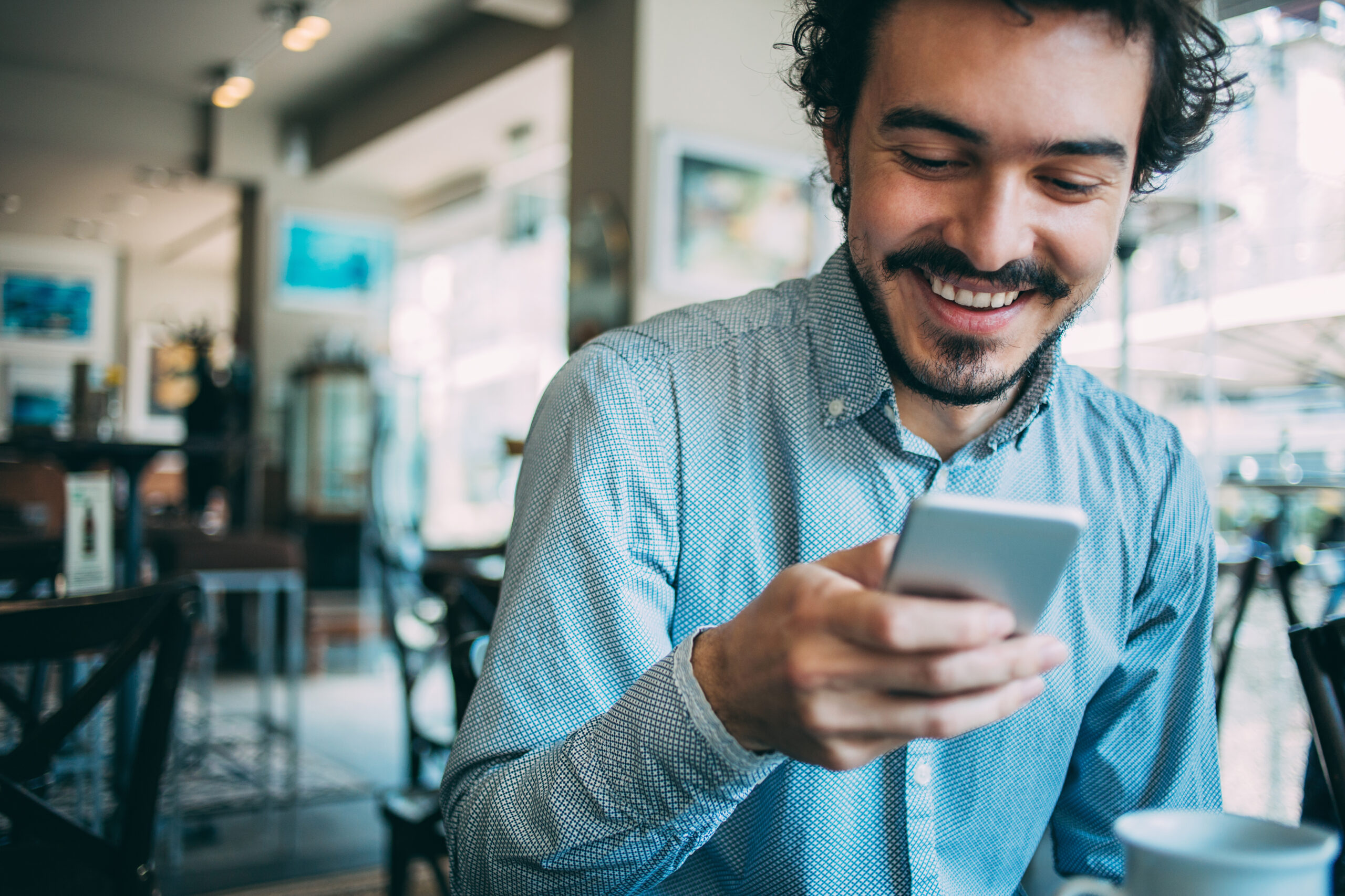 Young man sitting in cafe looking at his smart phone, with copy space.