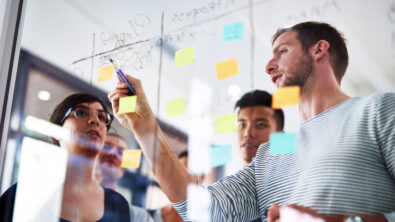 Cropped shot of coworkers using sticky notes on a glass wall during a meeting